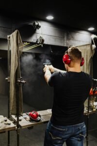 A man with ear protection shooting a pistol at a firing range indoors.
