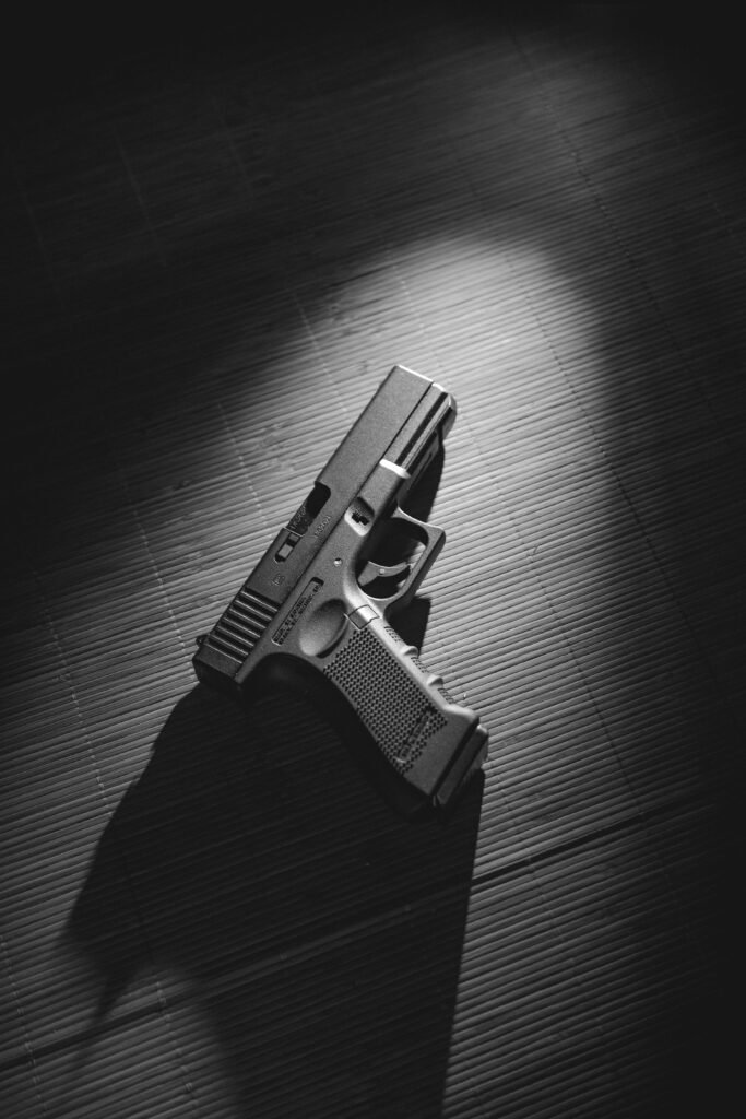 Black and white image of a handgun on a dark wooden surface with dramatic lighting.